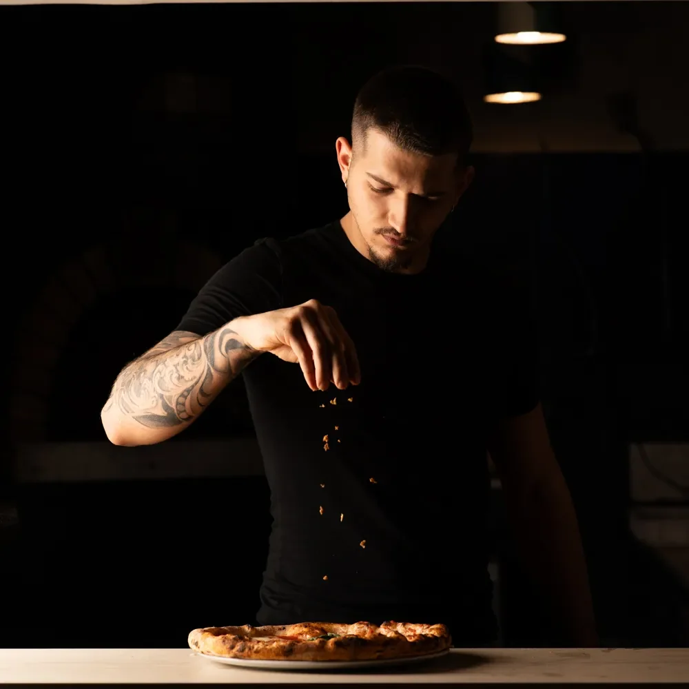 Mani che condiscono una pizza Monella con ingredienti freschi.