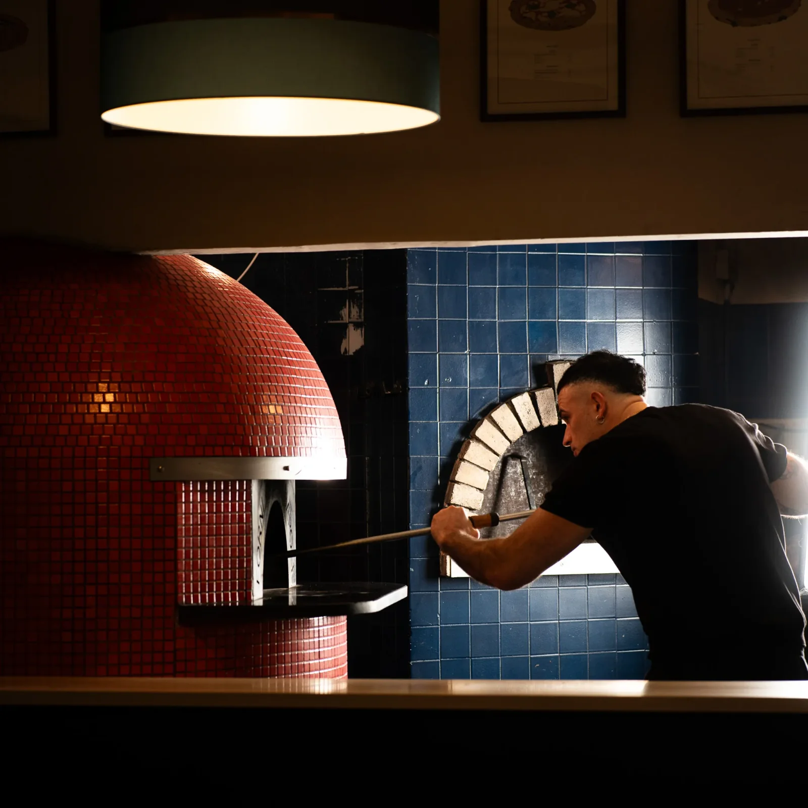 Il pizzaiolo di Monella inforna una pizza nel forno a legna.
